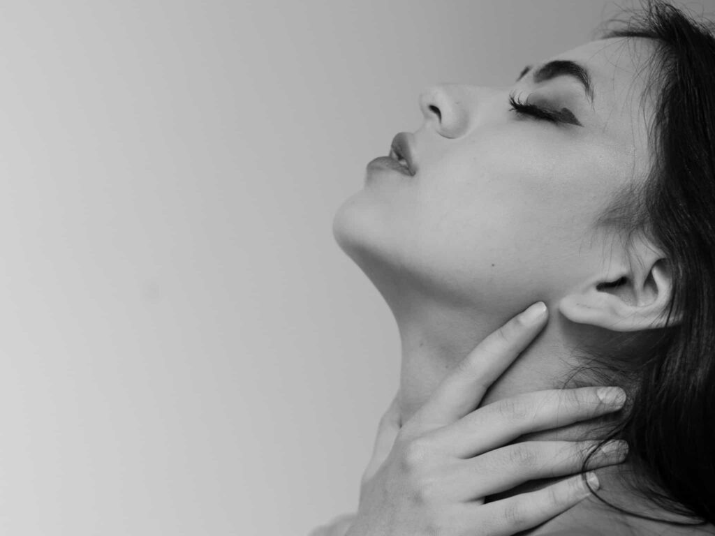 A woman in pain with her hands on her tight throat before she speaks.