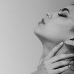 A woman in pain with her hands on her tight throat before she speaks.